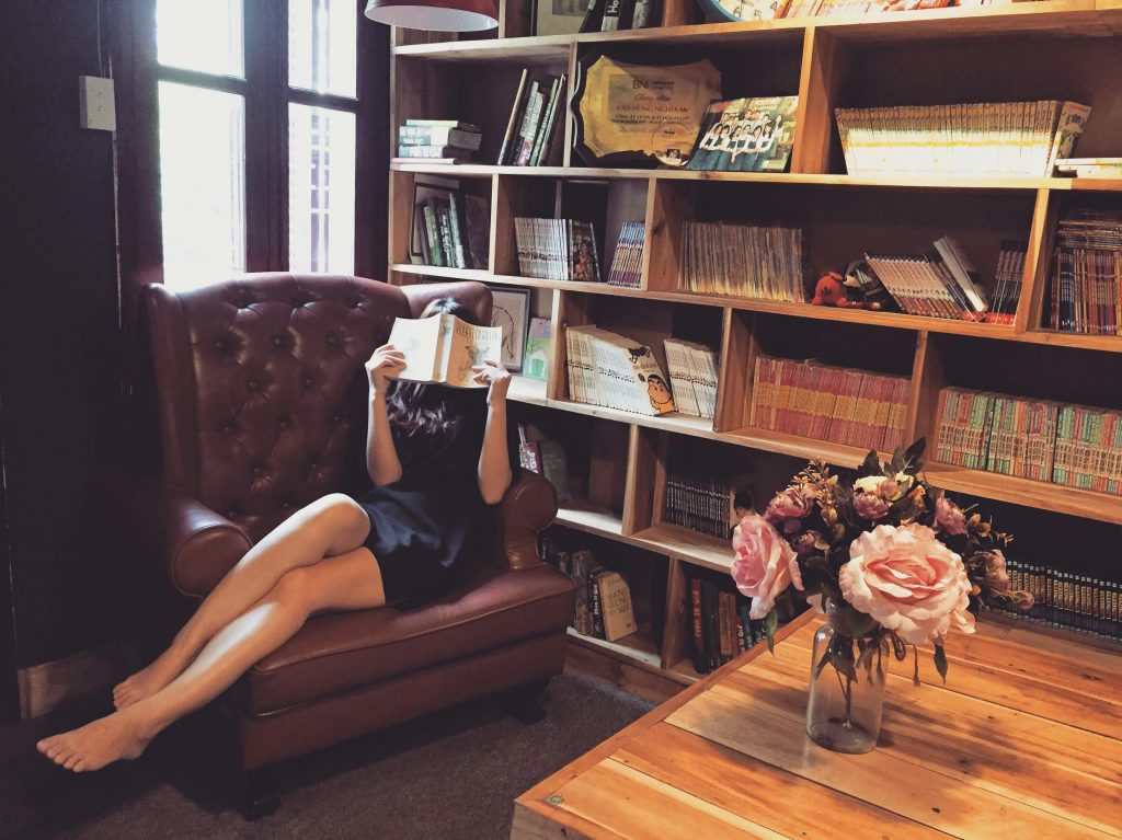Mulher lendo livro em sofá de couro com estante de madeira - cantinho de leitura elegante